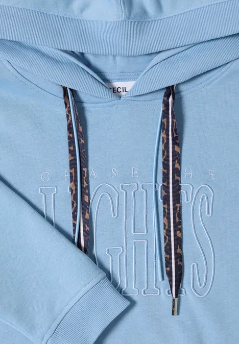 Sweatshirt mit Kapuze und Wording easy blue Nahaufnahme eines hellblauen Kapuzenpullovers mit geprägtem Schriftzug auf der Brust und gemusterten Tunnelzugbändern.