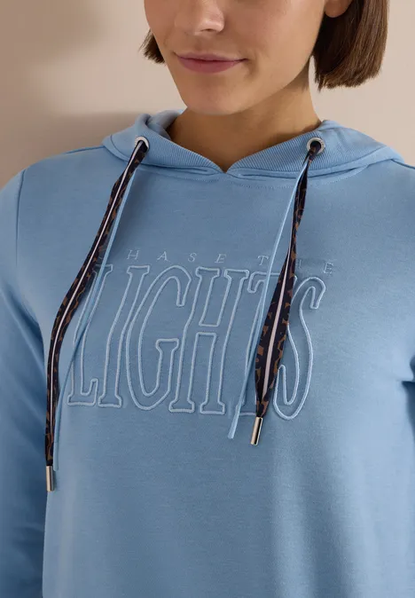 Sweatshirt mit Kapuze und Wording easy blue Person trägt hellblauen Kapuzenpulli mit weiß umrissenem 'LIGHTS'-Schriftzug und gestreiften Kordeln.