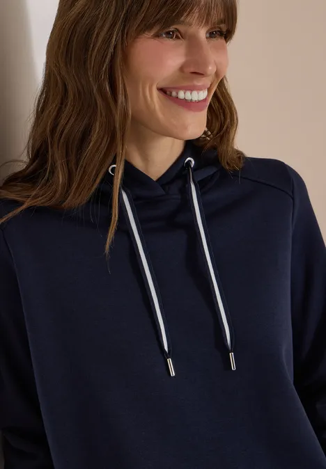 Frau in dunkelblauem Kapuzenpullover lächelt seitlich in die Kamera.