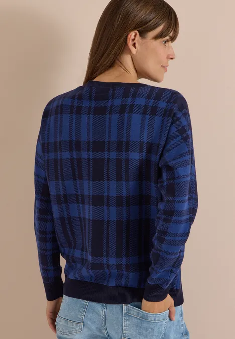 Sweter z rękawem typu dolman w kratkę urban dark blue Kobieta od tyłu w granatowym, w kratę swetrze i dżinsach, ręce w kieszeniach.