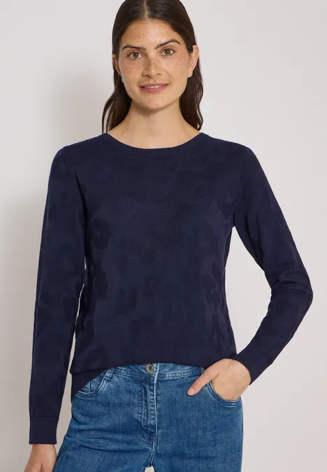 Trui met boothals en structuur urban dark blue Jonge vrouw met donker haar draagt een donkerblauw shirt met lange mouwen en een spijkerbroek, lachend voor een witte achtergrond.