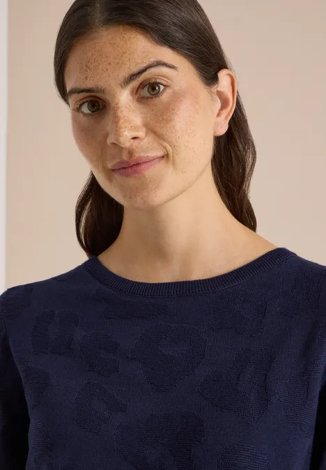 Trui met boothals en structuur urban dark blue Portret van een vrouw met donker haar en sproeten, in een marineblauwe trui tegen een beige achtergrond.