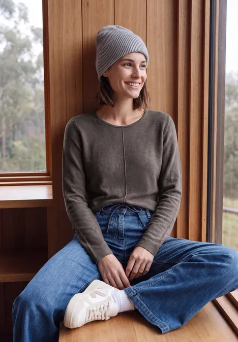Langarm Pullover mit Rundhals und Struktur mushroom taupe melange Junge Frau mit grauer Mütze und Pullover sitzt lächelnd in Jeans auf einer Fensterbank.