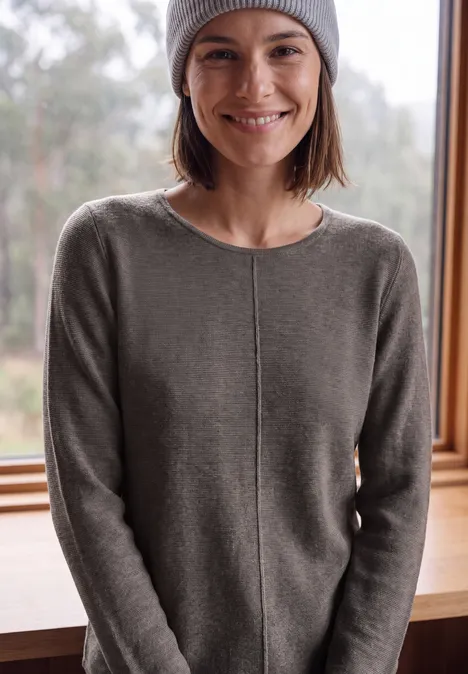 Langarm Pullover mit Rundhals und Struktur mushroom taupe melange Eine lächelnde Frau in einem grauen Pullover und Mütze steht vor einem Fenster mit Waldblick.