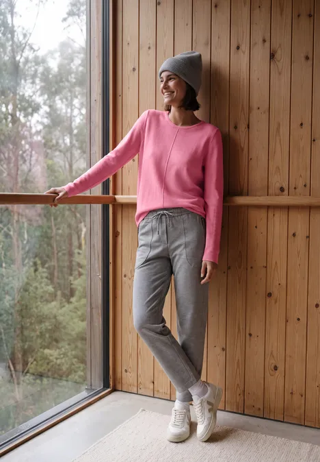 Langarm Pullover mit Rundhals und Struktur dark blossom melange Frau in pinkem Pullover, grauen Hosen und Mütze steht lässig am Fenster in hellem Holzraum.