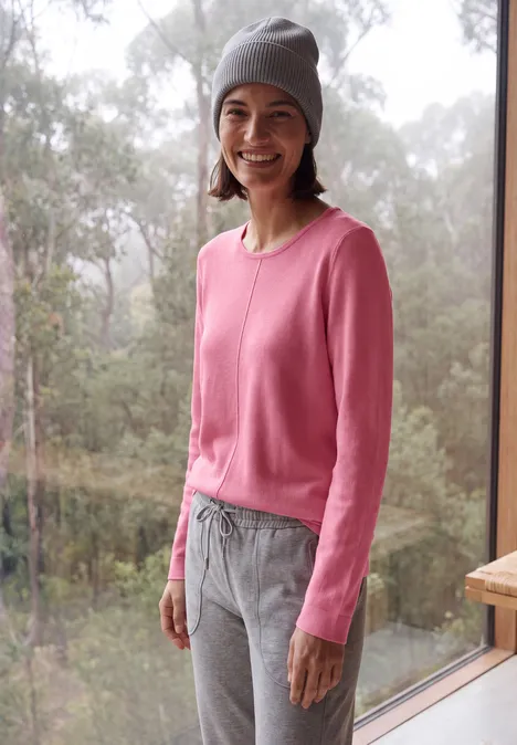 Langarm Pullover mit Rundhals und Struktur dark blossom melange Eine lächelnde Frau im rosa Pullover und grauen Hosen mit Mütze am Fenster, Wald im Hintergrund.