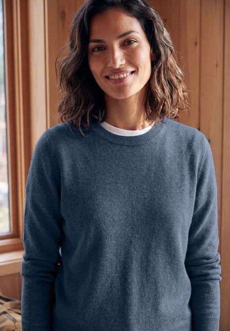 Pullover in Unifarbe mit Rundhals cotton blue melange Lächelnde Frau in blauem Pullover vor Holzwand
