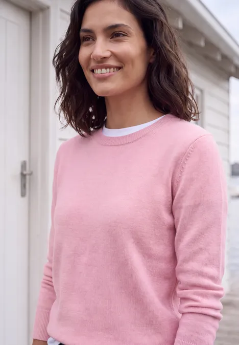 Pull uni à col rond mellow rose melange Une femme souriante portant un pull rose devant une porte blanche.