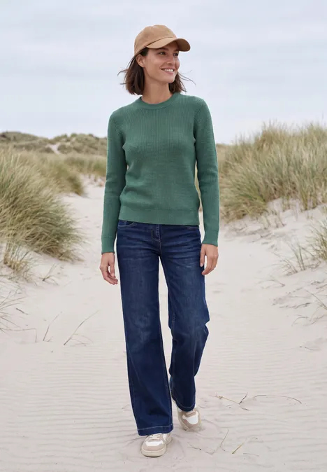 Pullover mit Rundhals und Struktur jewel green melange Frau in grünem Pullover und Jeans spaziert am Strand zwischen Dünen