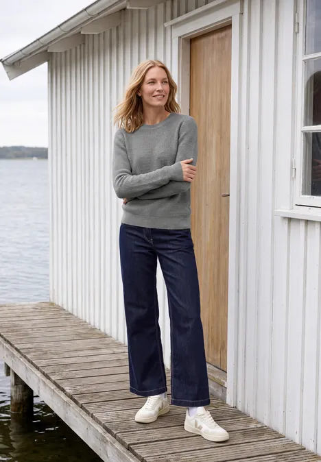 Pullover mit Rundhals und Struktur sporty grey melange Frau in grauem Pullover und weiten Jeans steht auf einem Steg vor einem weißen Holzhaus am Wasser.
