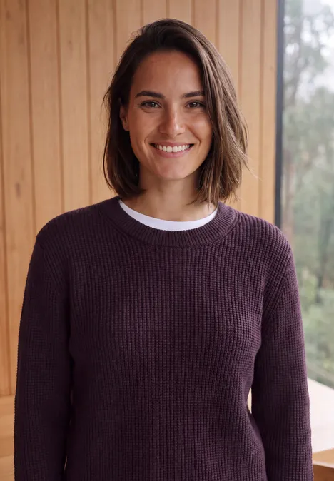 Pull à col rond et texturé eggplant red melange Femme souriante aux cheveux courts bruns portant un pull violet devant un mur en bois.