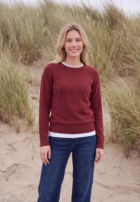 Pullover mit Rundhals und Strukturmix rhubarb melange Eine lächelnde Frau in rotem Pullover und Jeans steht am Strand vor hohen Dünengräsern.
