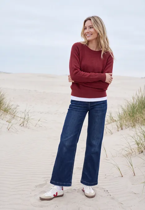 Pullover mit Rundhals und Strukturmix rhubarb melange Frau lächelt in rotem Pullover auf einer Dünenlandschaft am Strand.