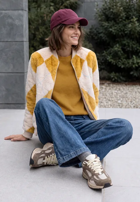 Pull col rond à textures contrastées golden honey melange Femme assise en extérieur, en jean, pull jaune, veste à losanges et casquette