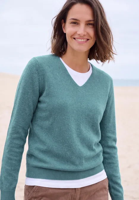 Langarm Pullover mit V-Neck multi lapis melange Lächelnde Frau im grünen Pullover und weißem T-Shirt am Strand.