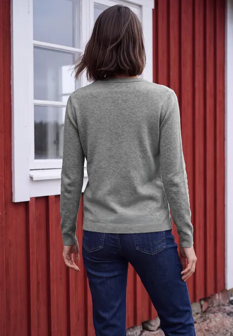 Langarm Pullover mit V-Neck sporty grey melange Eine Frau mit grauem Pullover und Jeans steht mit dem Rücken zur Kamera vor einer roten Holzfassade.