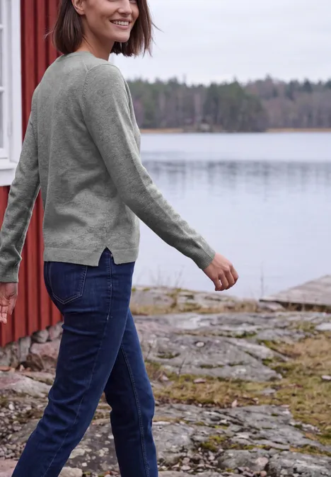 Langarm Pullover mit V-Neck sporty grey melange Frau in Jeans und Pullover spaziert am Seeufer neben einer roten Hütte.