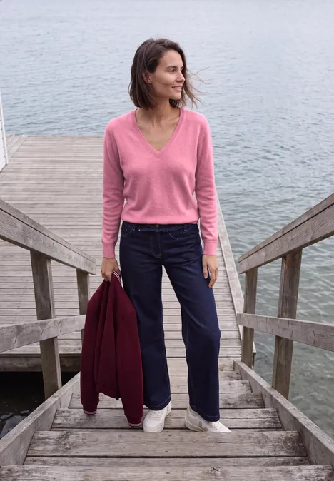 Langarm Pullover mit V-Neck dark blossom melange Eine Frau in rosa Pullover und Marinehose steht auf Holzstufen am Wasser und hält eine rote Jacke.
