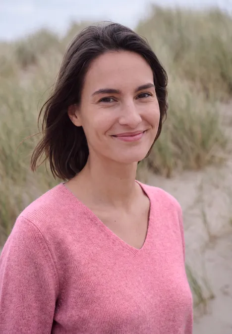 Langarm Pullover mit V-Neck dark blossom melange Eine lächelnde Frau in einem rosa Pullover vor Dünen am Strand
