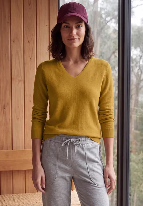 Femme en pull jaune et pantalon de jogging gris devant un mur en bois