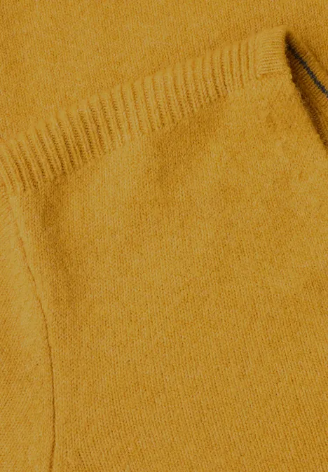 Gros plan sur un pull en maille jaune moutarde, poche apparente et trame fine.