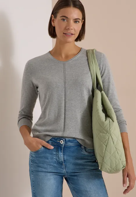 Basic Pullover mit V-Neck in Unifarbe mineral grey melange Eine Frau trägt einen grauen Strickpullover, blaue Jeans und eine olivgrüne Stepptasche über der Schulter.