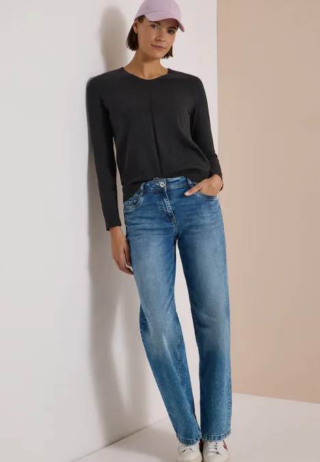 Pull couleur unie à col en V charcoal grey melange Femme appuyée contre un mur, pull noir, jean bleu et casquette rose.