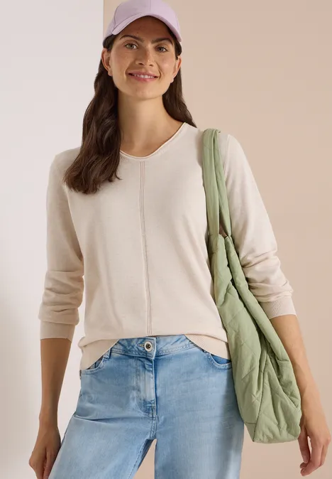 Lachende vrouw met lichte trui, jeans, paarse pet en groene gewatteerde tas.