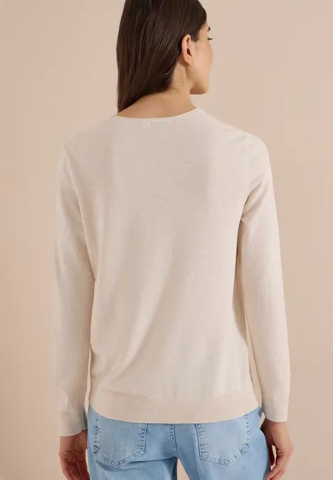 Vrouw van achteren in beige trui en blauwe jeans tegen lichte achtergrond.
