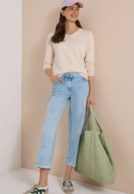 Vrouw in beige trui, wijd jeans, pet en grote groene gewatteerde shopper