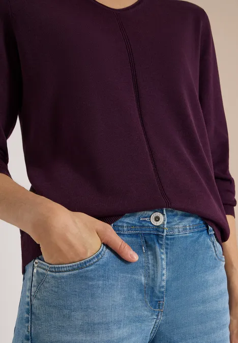 Paarse lange mouwen top en blauwe jeans, hand nonchalant in de zak.