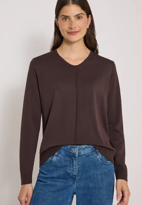 Eenvoudige trui met V-hals in effen kleur truffle brown Vrouw in bruin V-hals trui en blauwe spijkerbroek.