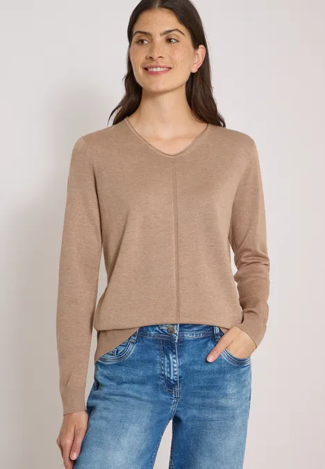 Eenvoudige trui met V-hals in effen kleur creamy mocha melange Een glimlachende vrouw draagt een bruine trui en een blauwe jeans.
