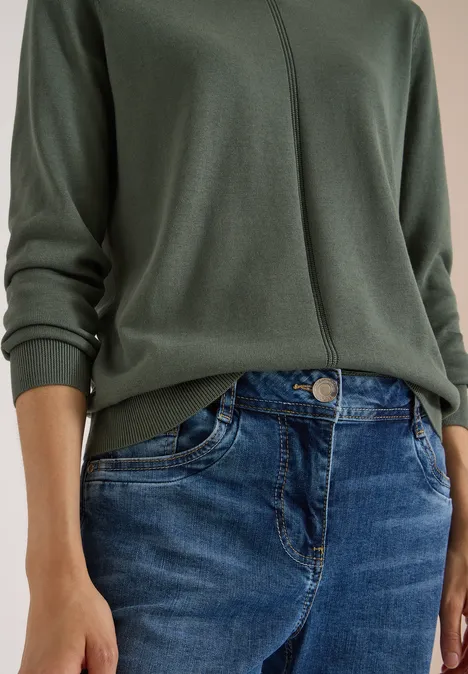 Eenvoudige trui met V-hals in effen kleur dried olive green Bovenlichaam van een persoon in een groen trui en blauwe spijkerbroek.