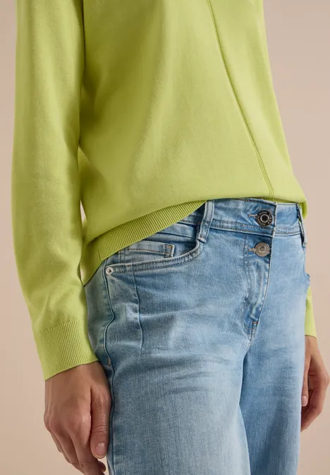 Eenvoudige trui met V-hals in effen kleur citrin green Persoon draagt een lichtgroene trui en lichtblauwe jeans, close-up van torso en armen.