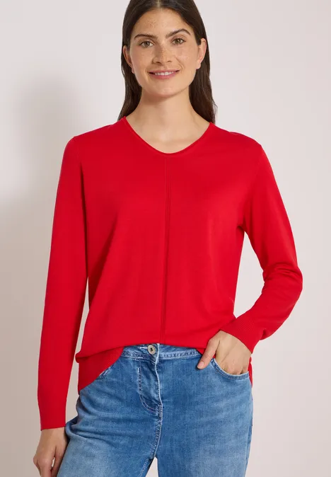 Eenvoudige trui met V-hals in effen kleur flame red Vrouw in rood V-hals trui en blauwe jeans, één hand in de zak.