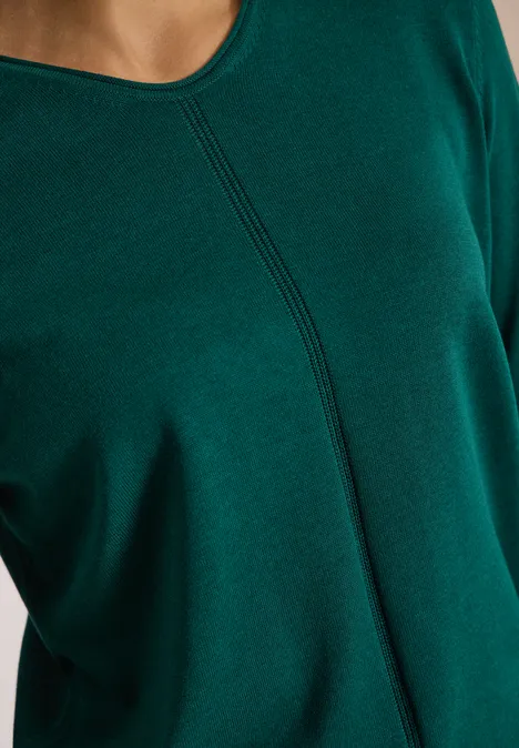 Pull couleur unie à col en V dark fir green Gros plan sur un haut vert foncé à col rond et détail décoratif