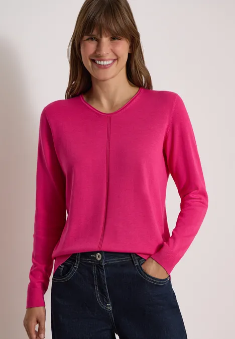 Basic Pullover mit V-Neck in Unifarbe pink flash Lächelnde Frau im pinken V-Pullover und dunklen Jeans, Hände in den Taschen.