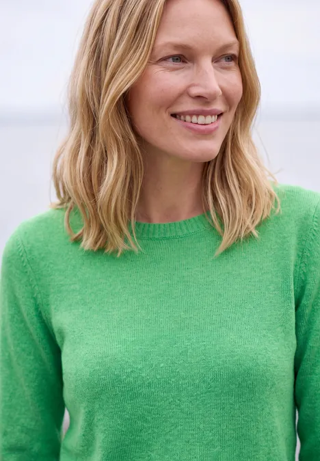 Pullover mit Boat Neck in Unifarbe celery green melange Eine lächelnde Frau mit mittellangem blonden Haar und grünem Pullover vor hellem Hintergrund.