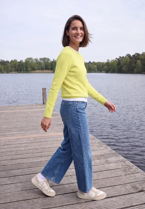 Pullover mit Boat Neck in Unifarbe iced yellow melange Eine Frau in gelbem Pullover und Jeans steht lächelnd auf einem Steg am See.