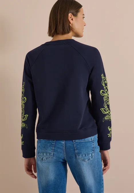 Sweatshirt mit Artwork am Ärmel urban dark blue Frau von hinten in dunkelblauem Sweatshirt mit grünen Ärmeldetails und blauen Jeans.