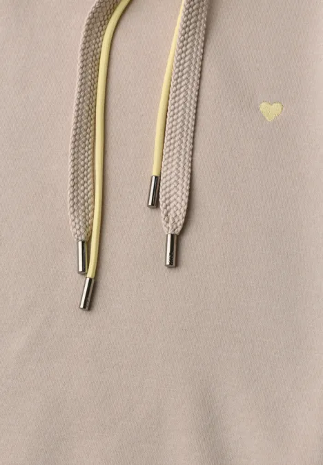 Gros plan sur un tissu beige avec deux cordons (beige et jaune) à embouts métalliques et un petit cœur doré.