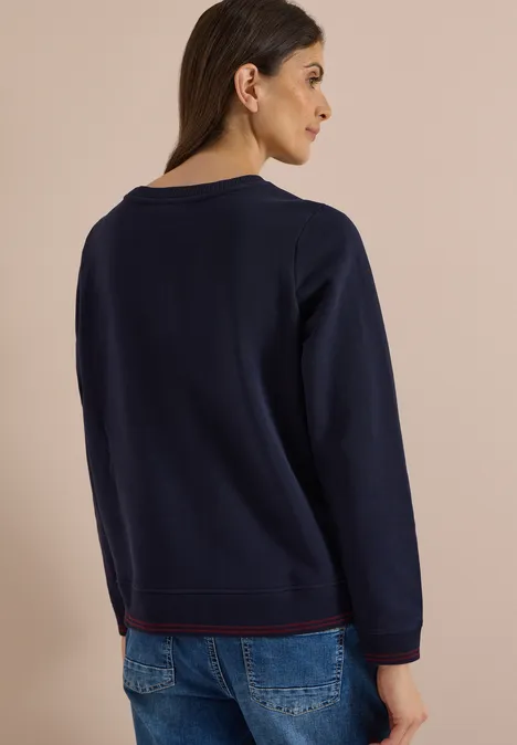 Sweatshirt mit Rundhals und Stickerei urban dark blue Frau mit dunklem Pullover und Jeans, Rückenansicht vor beigem Hintergrund