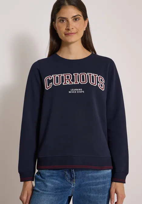 Sweatshirt mit Rundhals und Stickerei urban dark blue Junge Frau trägt dunkelblaue Sweatshirt mit Aufschrift 'CURIOUS', lächelt vor neutralem Hintergrund.