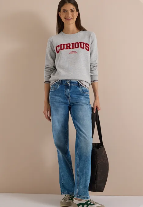 Sweatshirt mit Rundhals und Stickerei light grey melange Frau in grauem 'CURIOUS'-Pullover, blauen Jeans und schwarzer Tasche, lässiger Look vor neutralem Hintergrund.