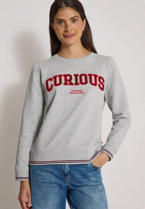 Sweatshirt mit Rundhals und Stickerei light grey melange Eine Frau trägt ein graues Sweatshirt mit rotem Schriftzug 'CURIOUS' und blaue Jeans.