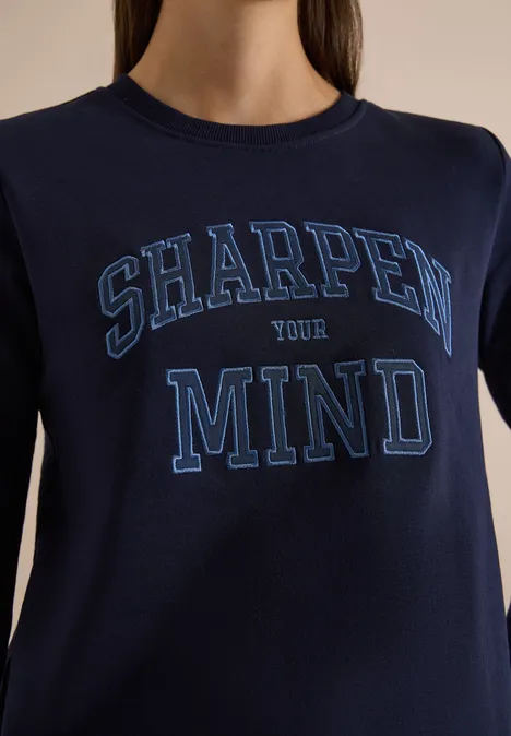Person trägt dunkelblaues T-Shirt mit der Aufschrift 'SHARPEN YOUR MIND'