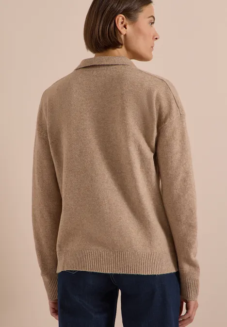 Frau von hinten mit beigem Pullover und dunkler Hose, Blick seitlich gerichtet.
