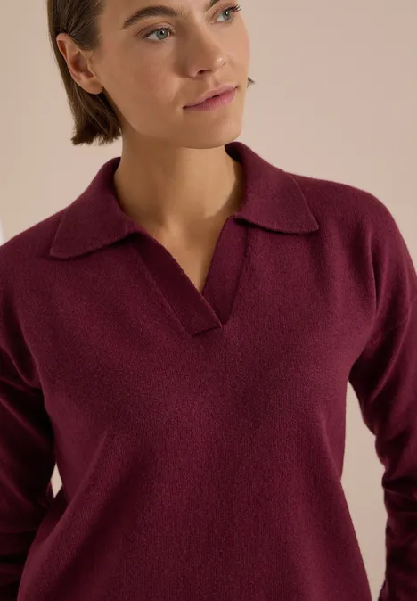 Eine Frau trägt einen burgunderfarbenen Pullover mit Polo-Kragen.