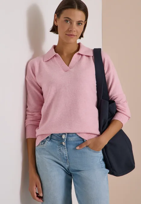 Trui met lange mouwen en polokraag mellow rose melange Een jonge vrouw draagt een roze polosweater, een spijkerbroek en een donkerblauwe tas over haar schouder.